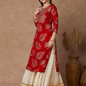 May include: A red and gold kurta with a leaf print and gold embroidery. The kurta is paired with a white layered skirt.