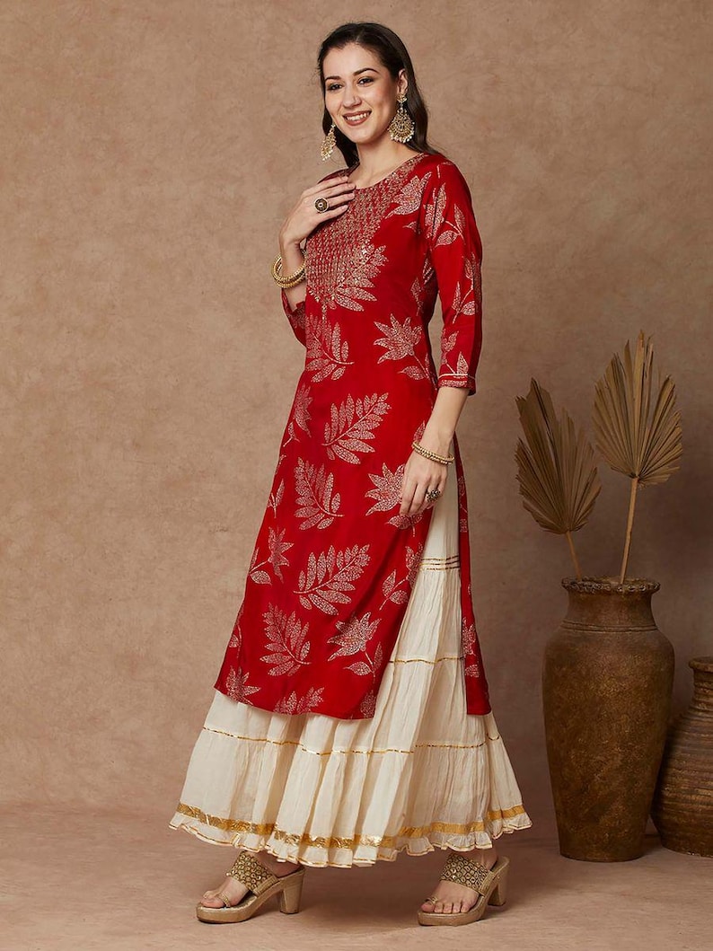 May include: A red and gold kurta with a leaf print and gold embroidery. The kurta is paired with a white layered skirt.