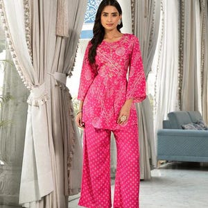 May include: A vibrant pink two-piece outfit featuring a tunic top and wide-leg pants. The top has long sleeves and intricate white patterns. The pants have a matching print. The outfit is suitable for casual or semi-formal occasions.