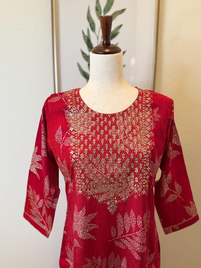 May include: A red kurta with a gold embroidered neckline and leaf pattern. The kurta is made of a soft, lightweight fabric and has a relaxed fit.