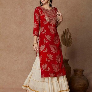 May include: A red long-sleeved kurta with a gold leaf print and gold embroidery around the neckline. The kurta is paired with a white layered skirt with gold trim.