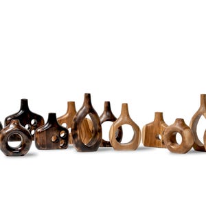 May include: A collection of wooden decorative vases in various shapes and sizes. The vases are made of different shades of wood, ranging from dark brown to light tan. Some have open circular or geometric cutouts.
