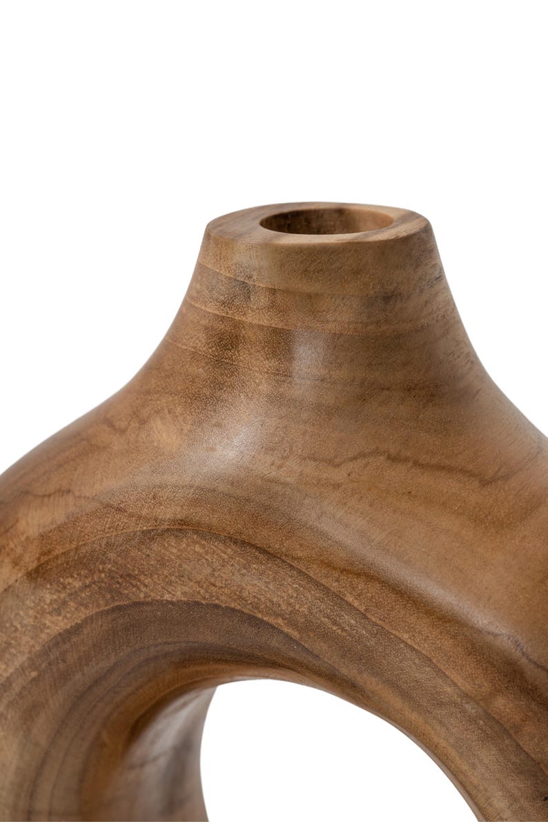 May include: A wooden decorative vase with a unique, open design. The vase is made of light brown wood and has a smooth, polished finish. The vase has a circular opening and a curved shape.