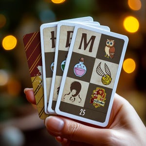 May include: A set of five playing cards featuring Harry Potter themed illustrations. The cards are numbered 25 and feature images of potions, a Gryffindor crest, and a magical creature.