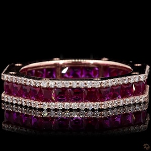 Pode incluir: Anel de ouro rosa com rubis de corte quadrado e pequenos diamantes. O anel apresenta três fileiras de rubis vermelhos escuros de corte quadrado, separadas por fileiras de pequenos diamantes brilhantes. O anel está sobre um fundo preto.