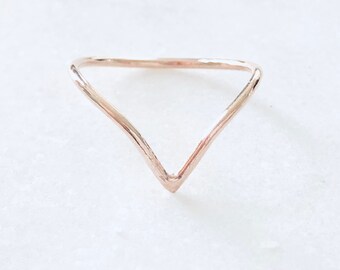 May include: A simple, minimalist gold ring with a V-shaped design. The ring is made of a thin, delicate wire and has a hammered finish.