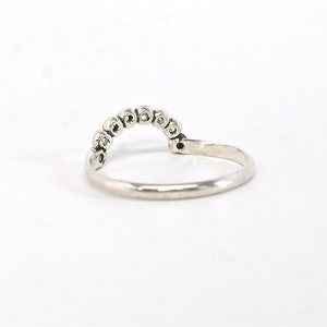 May include: A silver ring with a row of small, clear stones set in a curved shape.