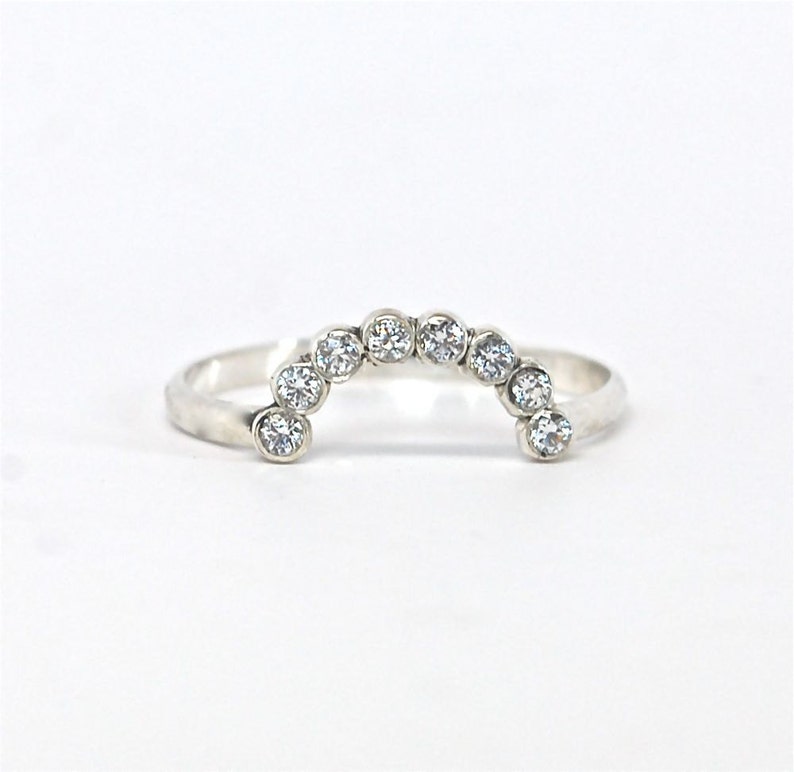 May include: A silver ring with a row of clear round stones set in a curved arch shape.
