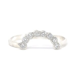 May include: A silver ring with a row of small, round, clear stones set in a curved arch shape.