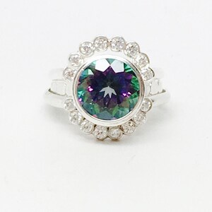 May include: A silver ring with a large, round, iridescent gemstone surrounded by a halo of smaller clear gemstones.