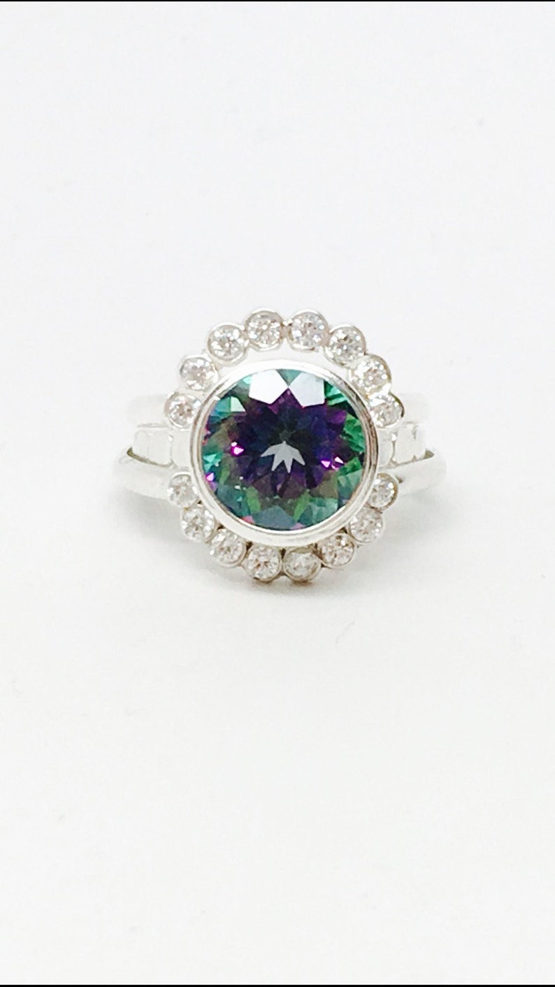 May include: A silver ring with a large, round, iridescent gemstone surrounded by a halo of smaller clear gemstones.