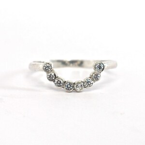 May include: A silver ring with a curved band and a row of small, clear gemstones.