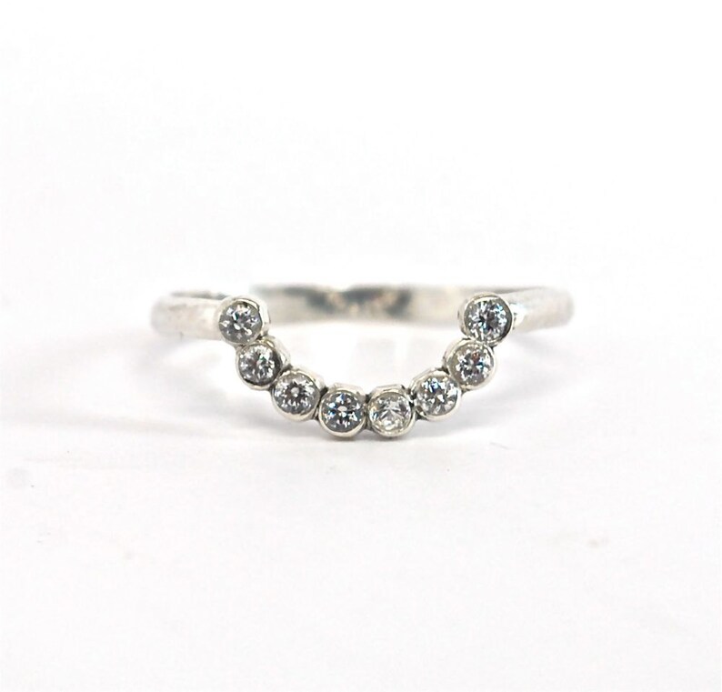 May include: A silver ring with a curved band and a row of small, clear gemstones.