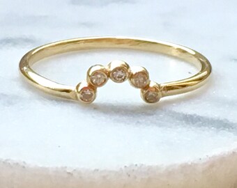 May include: A gold band ring with a row of small, round diamonds set in a curved arch shape.