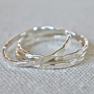 May include: Three silver hammered stacking rings. The rings are simple and delicate, with a textured finish.
