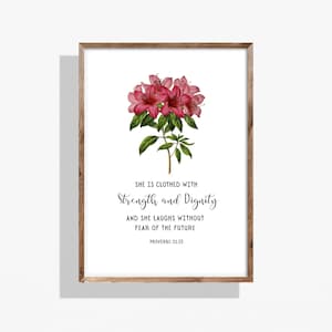 May include: A framed print with a watercolour illustration of pink flowers and green leaves. The text reads "SHE IS CLOTHED WITH STRENGTH AND DIGNITY AND SHE LAUGHS WITHOUT FEAR OF THE FUTURE PROVERBS 31:25". The frame is made of wood.