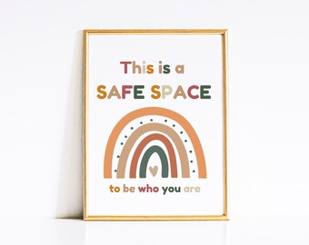 May include: A framed print with a rainbow design in shades of orange, brown, red, and green. The rainbow has a small heart in the center. The text "This is a SAFE SPACE to be who you are" is printed in colorful letters.