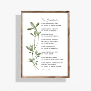 May include: Framed print featuring "The Beatitudes" text with a watercolor botanical illustration. The text is in a classic font, and the frame is a natural wood tone. The artwork is suitable for home decor.