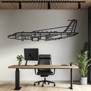 May include: A black metal wall art piece shaped like the side profile of a commercial airplane. The design features a detailed outline of the fuselage, wings, tail section, and jet engines, mounted horizontally on a plain light-colored wall.