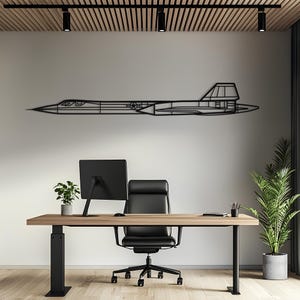 Op de afbeelding: Een zwart metalen wanddecoratie in de vorm van het zijprofiel van een Lockheed SR-71 Blackbird vliegtuig. Het ontwerp heeft een dun, lineair silhouet met een spitse neus, een cockpitsectie, een staartvin en een klein ster-insigne.