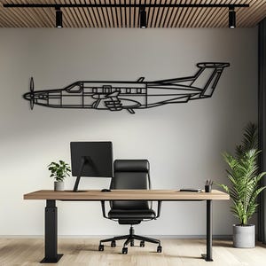 Könnte beinhalten: Ein schwarzes Wandkunstobjekt aus Metall in Form eines einmotorigen Turboprop-Flugzeugs. Das Design zeigt das Seitenprofil des Flugzeugs mit einem Propeller an der Vorderseite, einem Cockpitfenster, einem Rumpf, Flügeln und einem Heckteil.