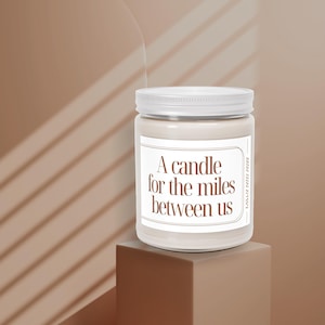 May include: A white candle with a brown label that reads "A candle for the miles between us".