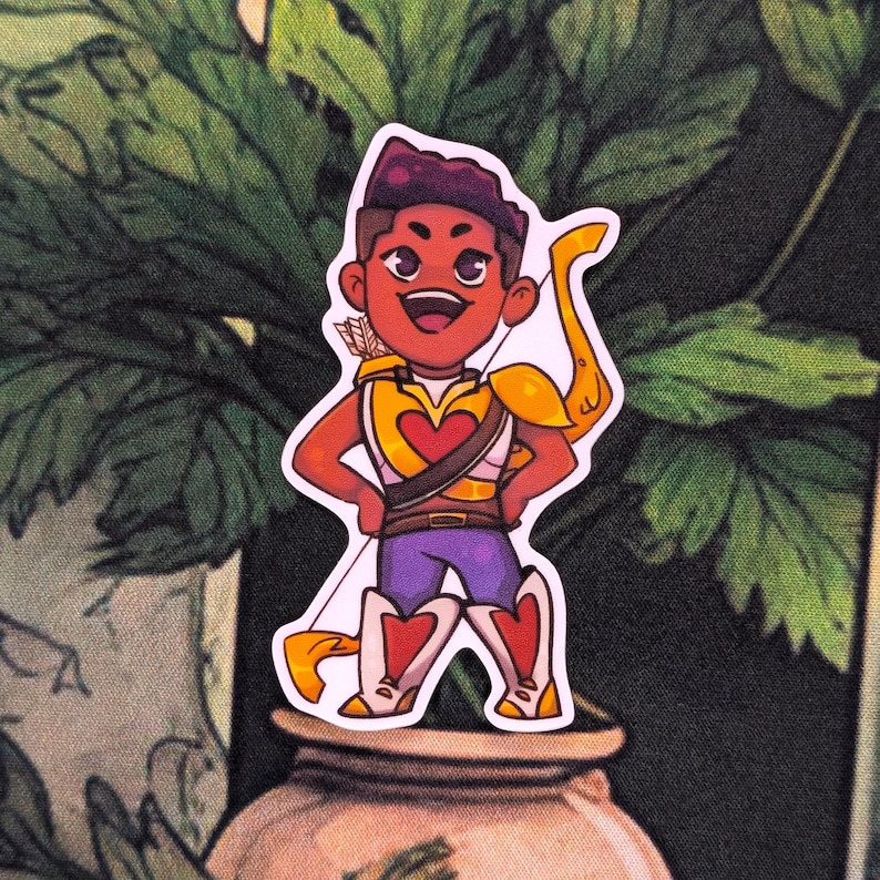 Pode incluir: Um adesivo com um personagem de desenho animado com pele castanha, vestindo uma roupa amarela e dourada com um design de cora&ccedil;&atilde;o. O personagem est&aacute; segurando um arco e flecha. O fundo &eacute; um padr&atilde;o floral verde escuro e marrom.