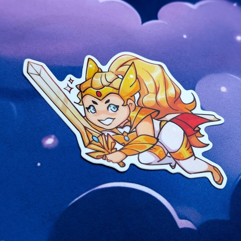 Pode incluir: Um adesivo com uma ilustra&ccedil;&atilde;o de desenho animado de um personagem com cabelo loiro, uma coroa dourada e uma espada dourada. O personagem est&aacute; vestindo uma roupa dourada e branca com uma capa vermelha. O fundo &eacute; um c&eacute;u azul e roxo com nuvens.