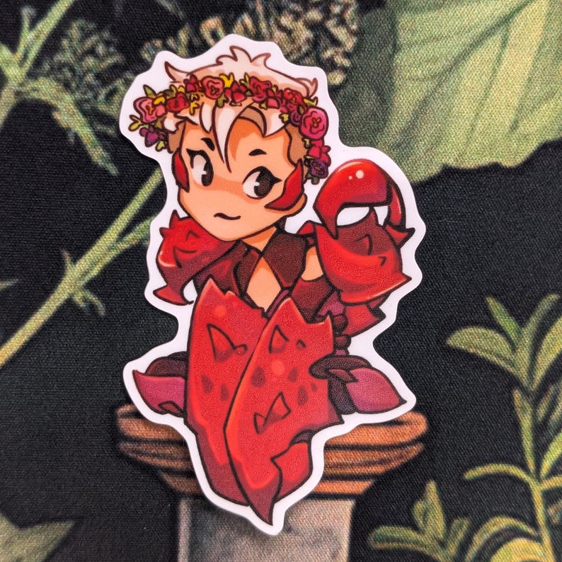 Pode incluir: Um adesivo com um personagem de desenho animado com uma armadura vermelha em forma de caranguejo e uma coroa de flores. O personagem tem pele clara e cabelo loiro claro. Fundo escuro com folhagem verde.