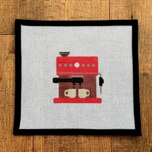May include: A needlepoint canvas featuring a red espresso machine with two cups. The machine has a dark brown base and black details. The canvas is bordered by a black fabric.