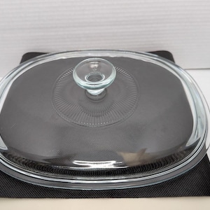 以下が含まれることがあります： 丸いハンドルが付いた透明なガラス製の楕円形キャセロール皿の蓋。蓋の中央には装飾的な模様があり、縁は丸みを帯びています。蓋はキャセロール皿に合うように設計されています。