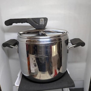 May include: A stainless steel pressure cooker with black handles. The pot has a shiny, reflective surface and a lid with a pressure release valve. The cooker is designed for efficient cooking, ideal for the kitchen.