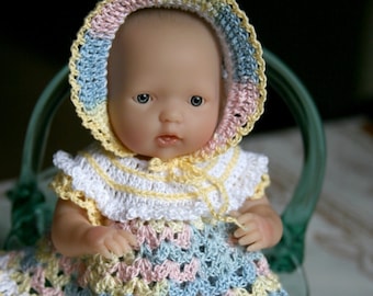 May include: A crocheted doll wearing a pastel-colored dress and matching hat. The doll has a light-skinned complexion and blue eyes.