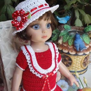 Può includere: Una bambola che indossa un vestito rosso all'uncinetto con bordi bianchi e un cappello bianco all'uncinetto con un fiore rosso e bianco a pois.