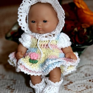 May include: A small crocheted doll wearing a white crocheted dress with pink, yellow, and blue stripes. The doll has a crocheted hat and booties.