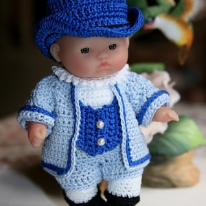 May include: A crocheted doll wearing a blue hat and a blue and white crocheted outfit. The doll has a light complexion and blue eyes.