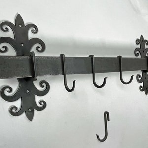 May include: Black metal pot rack with decorative scrollwork on the ends. The rack has five hooks for hanging pots and pans.