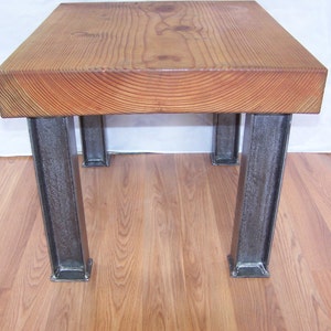 May include: A square wooden coffee table with a natural wood finish and four metal legs. The legs are made of a dark metal and have a rectangular shape.