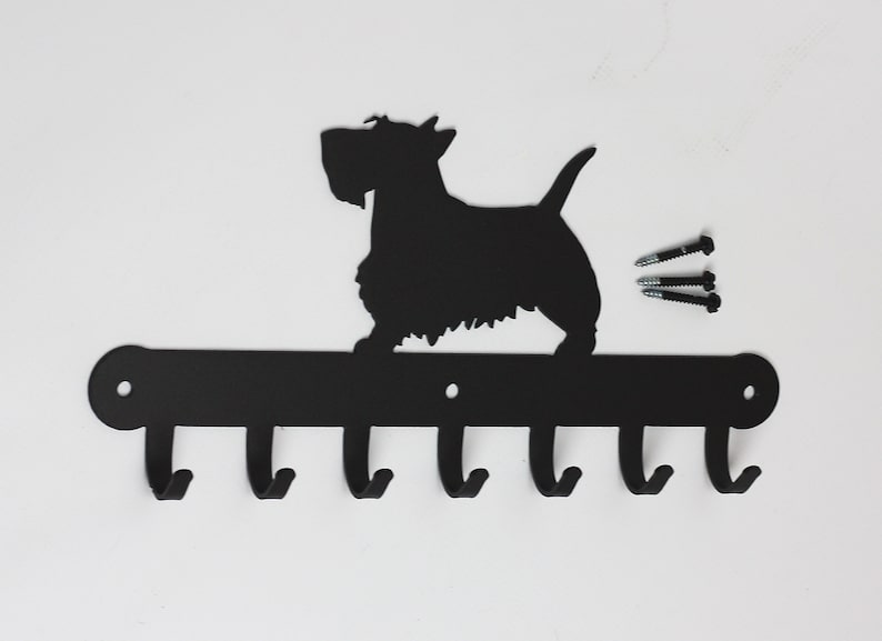 May include: Black metal key holder with a silhouette of a Scottish Terrier dog. The holder has six hooks and comes with screws for mounting.