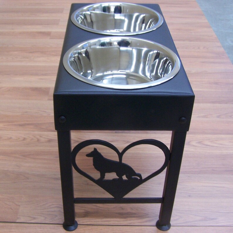 Pode incluir: Suporte para comida de c&atilde;o de metal preto com duas tigelas de a&ccedil;o inoxid&aacute;vel e um recorte em forma de cora&ccedil;&atilde;o com a silhueta de um pastor alem&atilde;o.