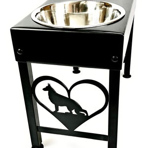 Pode incluir: Suporte para tigelas de c&atilde;o de metal preto com duas tigelas de a&ccedil;o inoxid&aacute;vel. O suporte apresenta um recorte em forma de cora&ccedil;&atilde;o com uma silhueta de um pastor alem&atilde;o.