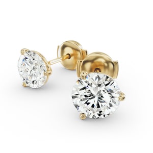 May include: A pair of gold stud earrings with large, round, clear gemstones. The earrings have a classic three-prong setting and a post and butterfly backing. The gold has a polished finish, and the gemstones sparkle brightly against the white background.