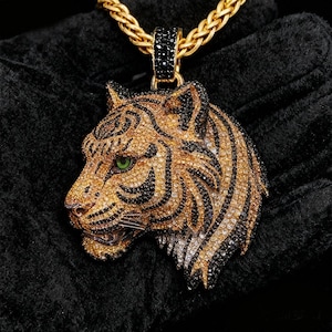 May include: Gold-toned tiger pendant necklace with black and clear crystal accents. The tiger's head features green eyes and black stripes. The necklace has a gold chain.