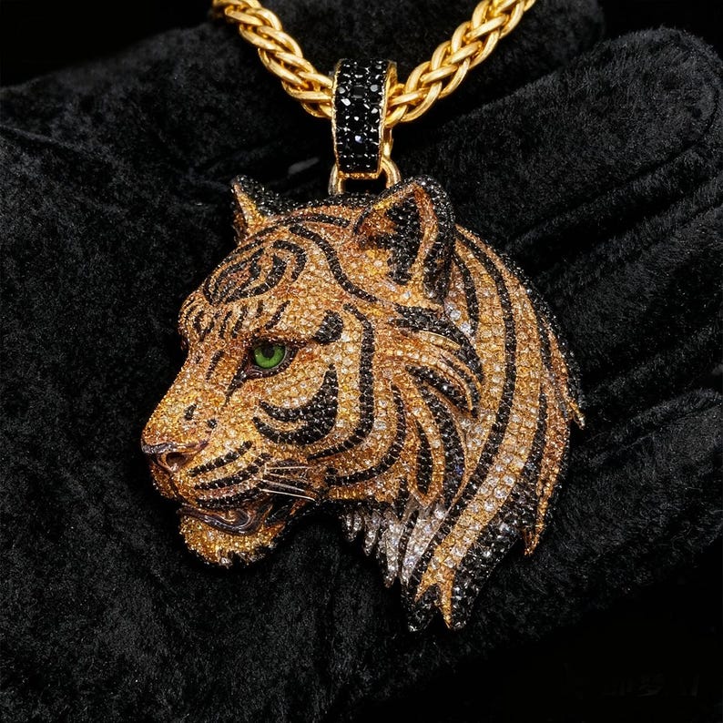 May include: Gold-toned tiger pendant necklace with black and clear crystal accents. The tiger's head features green eyes and black stripes. The necklace has a gold chain.