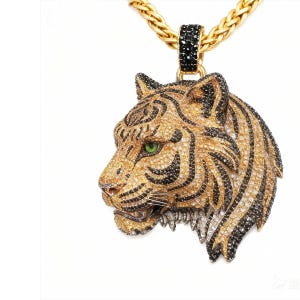May include: Gold-toned tiger pendant necklace with black and clear crystal accents. The tiger's head features a detailed design with black stripes, a green eye, and a gold chain. The pendant is attached to a gold chain.