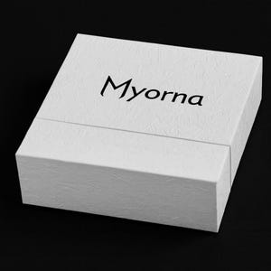 May include: A white textured box with the word "Myorna" printed in black on the top. The box is rectangular and has a lid that fits over the base. The background is black.