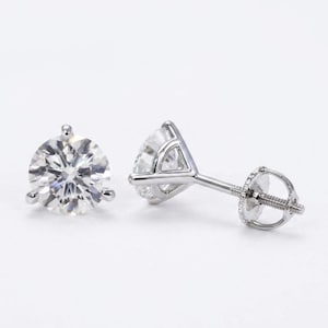 May include: A pair of sparkling round-cut diamond stud earrings. Each earring features a brilliant, clear gemstone set in a silver-colored, three-prong setting with a screw-back closure. The earrings are displayed against a white background.