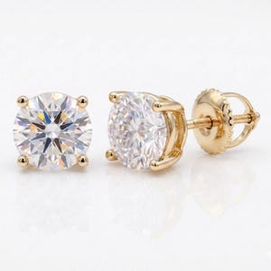 May include: A pair of round-cut diamond stud earrings with a gold setting. The earrings feature a brilliant, clear gemstone held in place by four prongs. The post and backing are also gold.