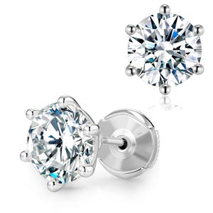 May include: Two silver stud earrings with a large, clear, round-cut gemstone. Each earring features a six-prong setting, showcasing the brilliant facets of the stone. The earrings are set against a white background.
