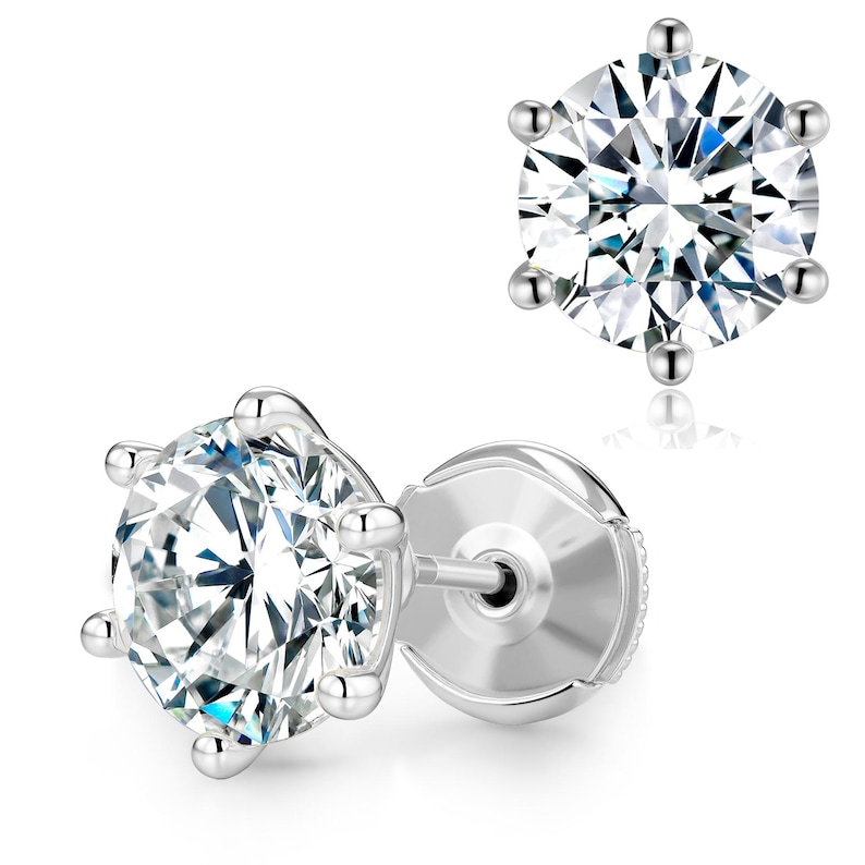 May include: Two silver stud earrings with a large, clear, round-cut gemstone. Each earring features a six-prong setting, showcasing the brilliant facets of the stone. The earrings are set against a white background.